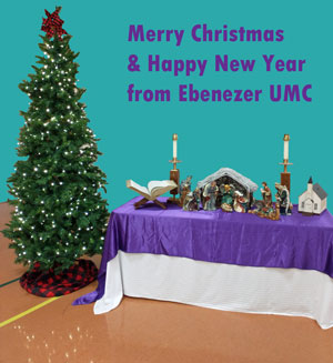 Picture of lit Christmas tree next to table with nativity scene with words at top of photo Merry Christmas and Happy New Year from Ebenezer UMC